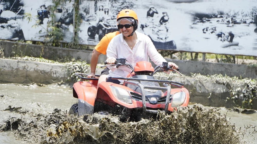 ATV blasting through a muddy water pit with wheels kicking up rich brown spray