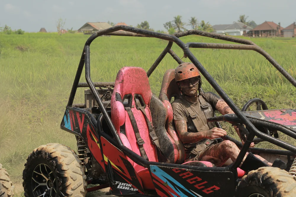 Mud-splattered rider smiling from the buggy driver seat after the muddy trail