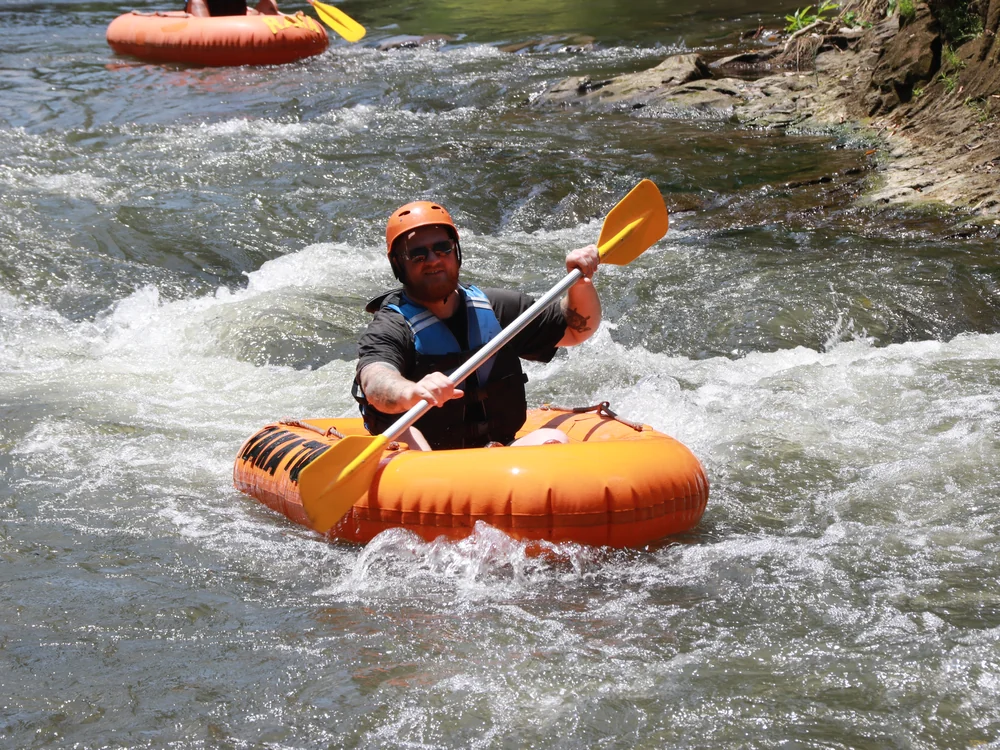 River tubing rider navigating foaming white water rapids with paddle raised